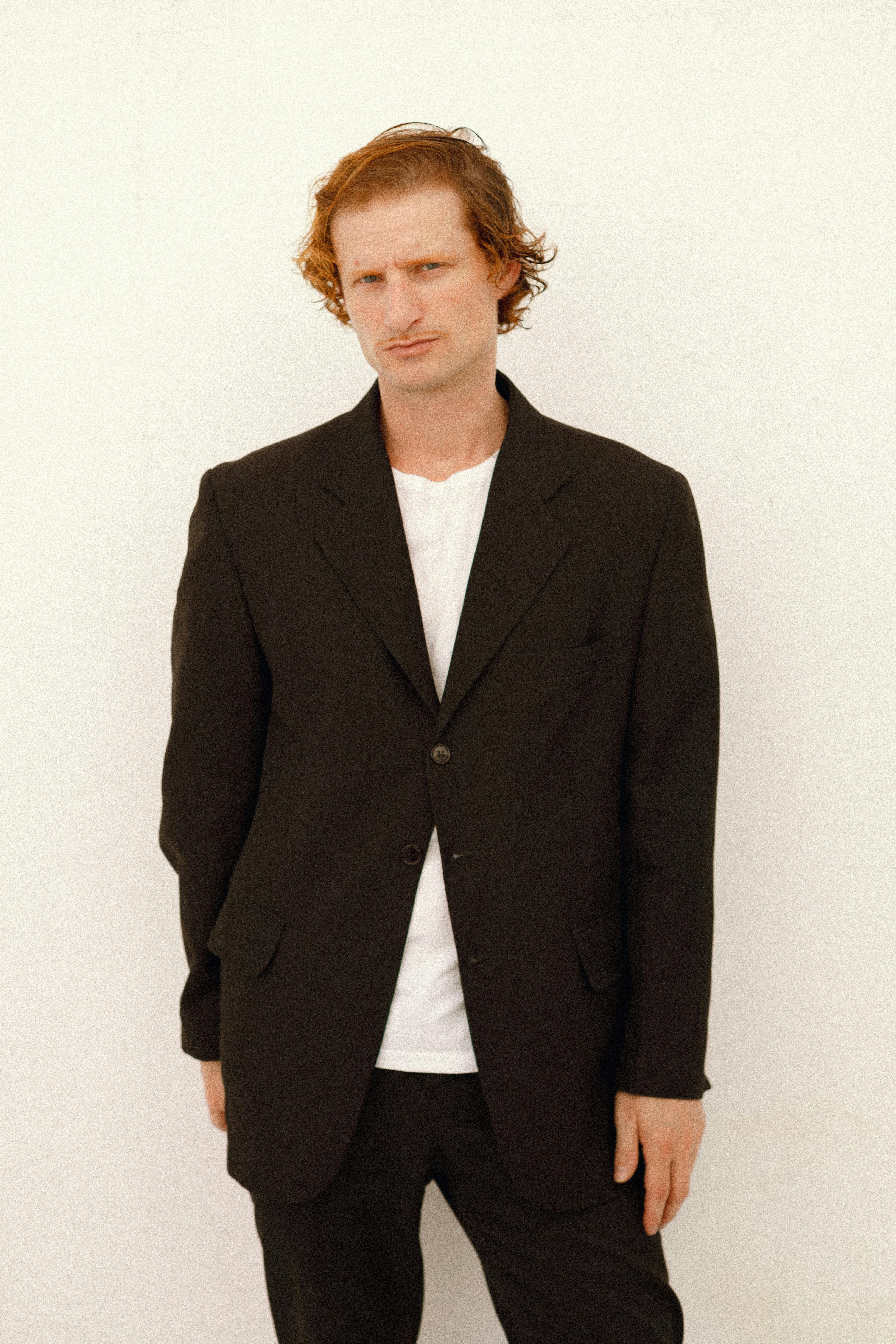 A relaxed portrait of a man wearing a black blazer against a plain backdrop.