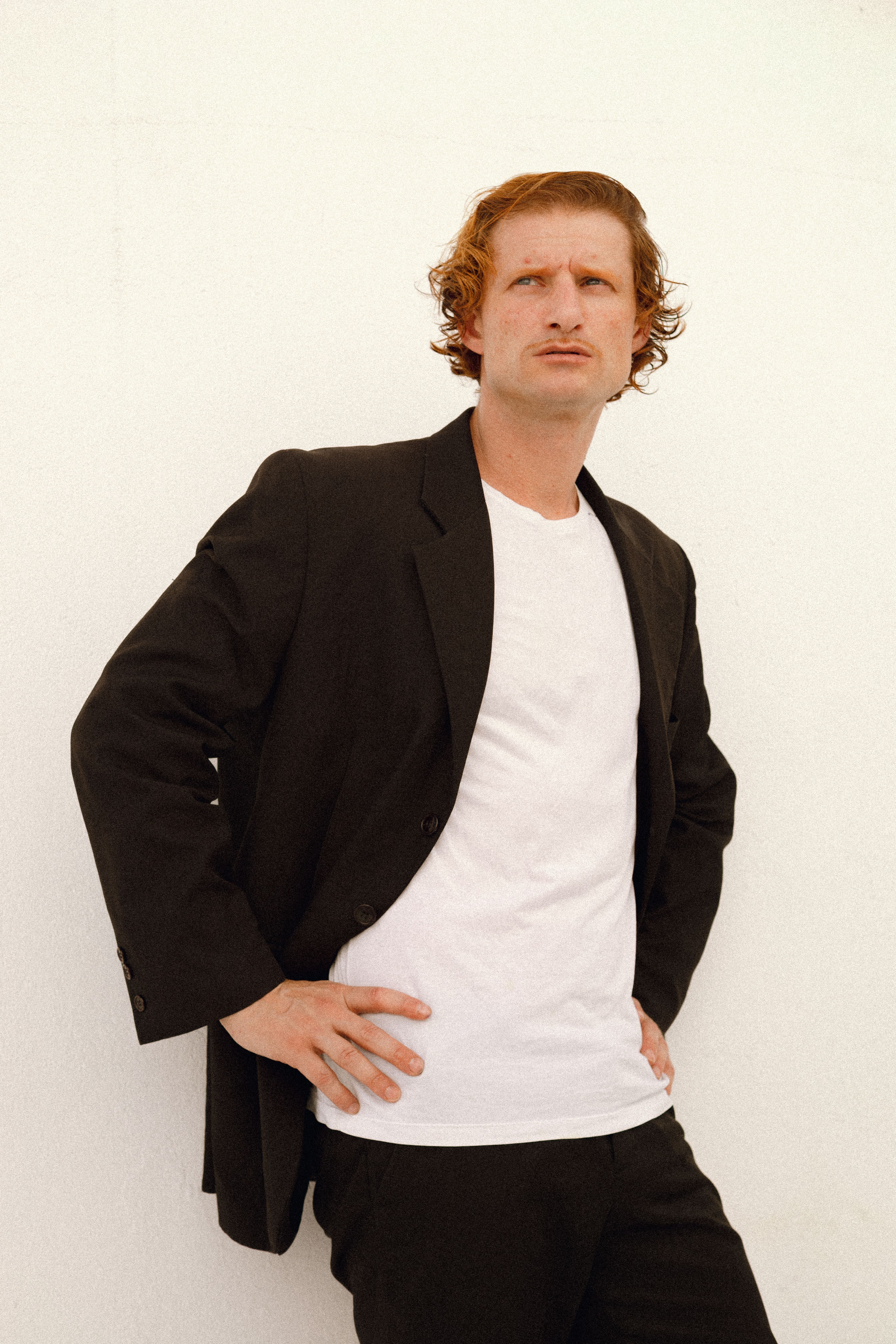 Portrait of a man wearing a black suit and white shirt, standing confidently against a white background.