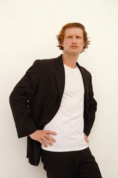 Portrait of a man wearing a black suit and white shirt, standing confidently against a white background.