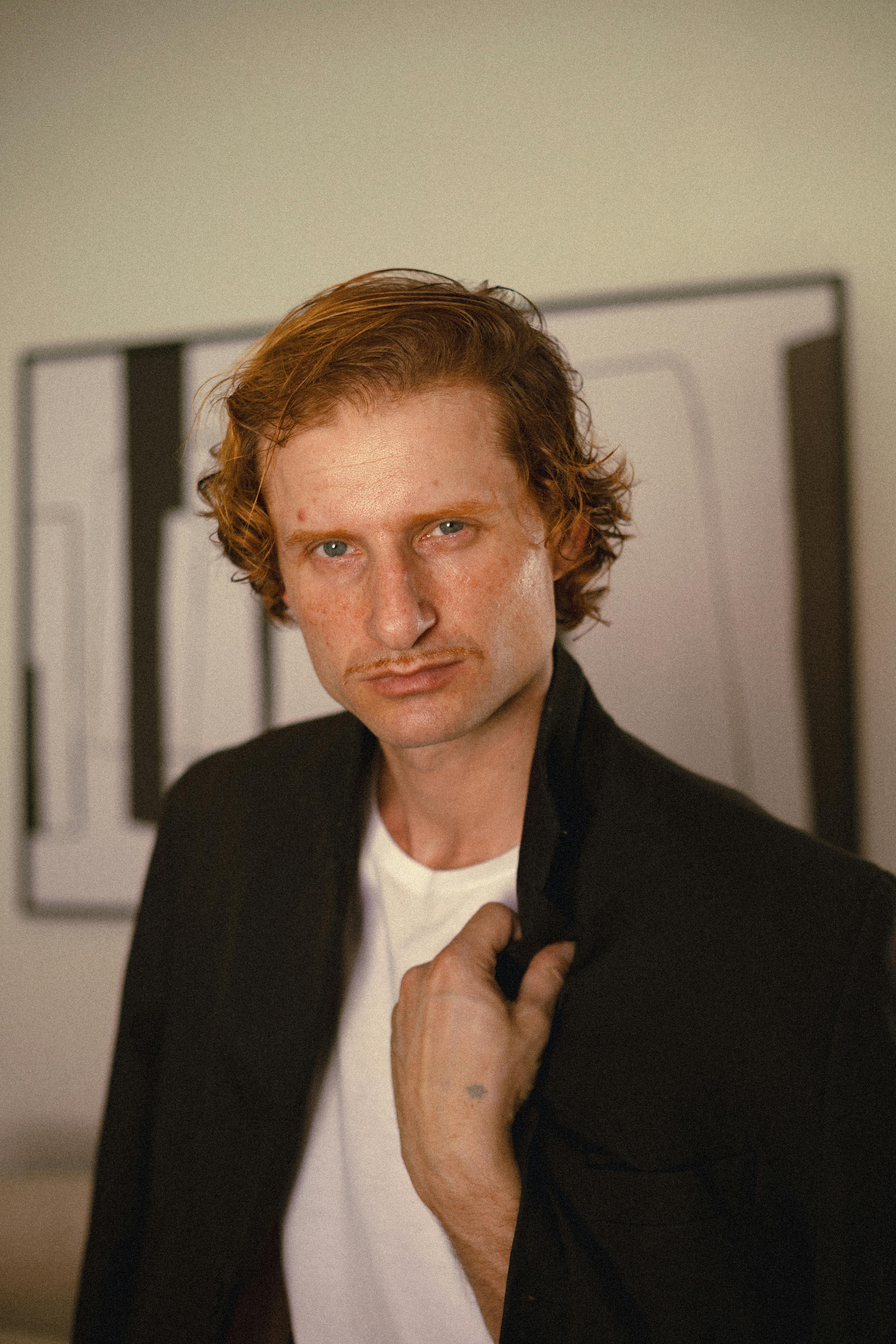 Close-up portrait of an adult male with red hair in a studio setting, showcasing confidence.