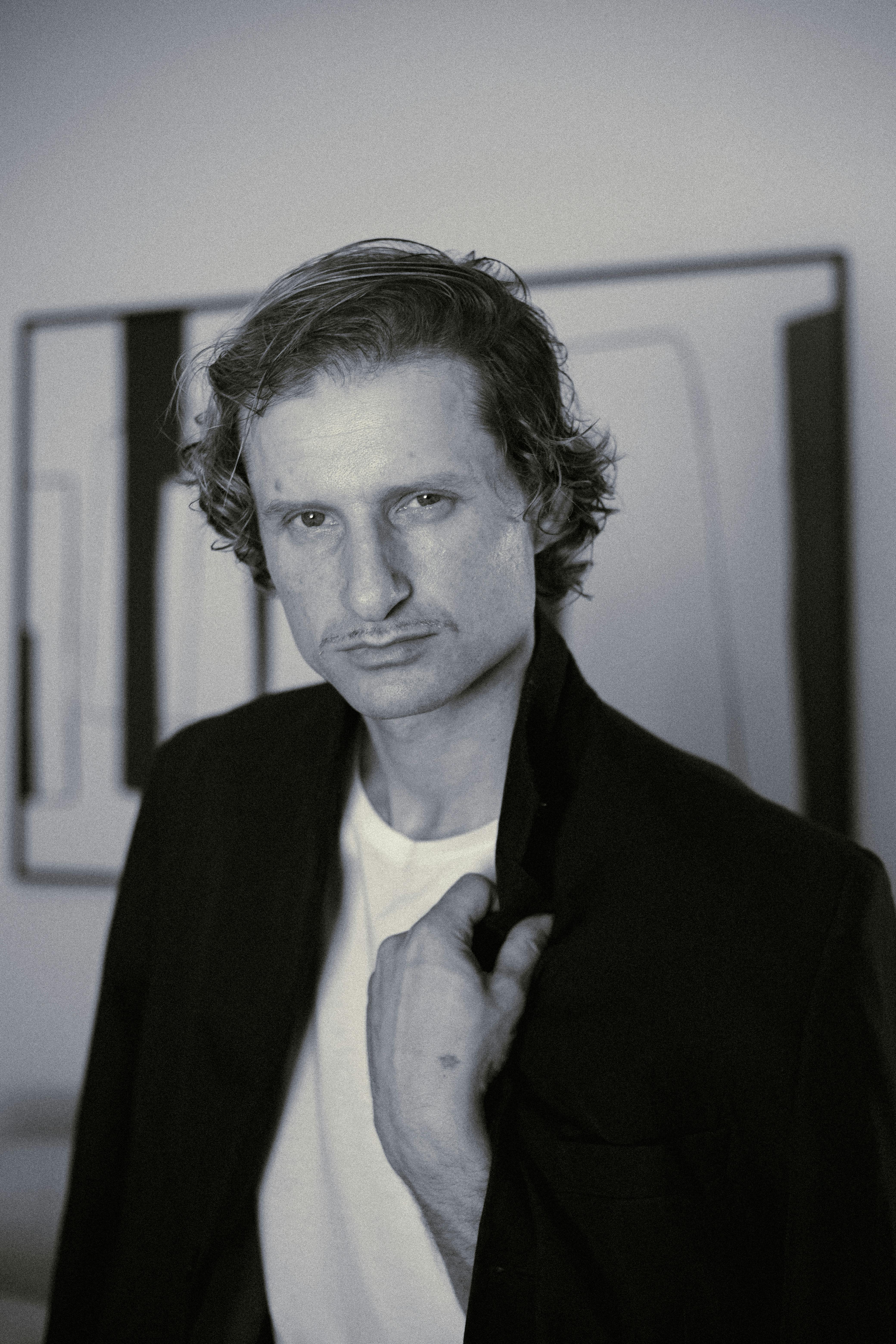 Expressive black and white portrait of a man wearing a suit jacket indoors, creating a vintage mood.