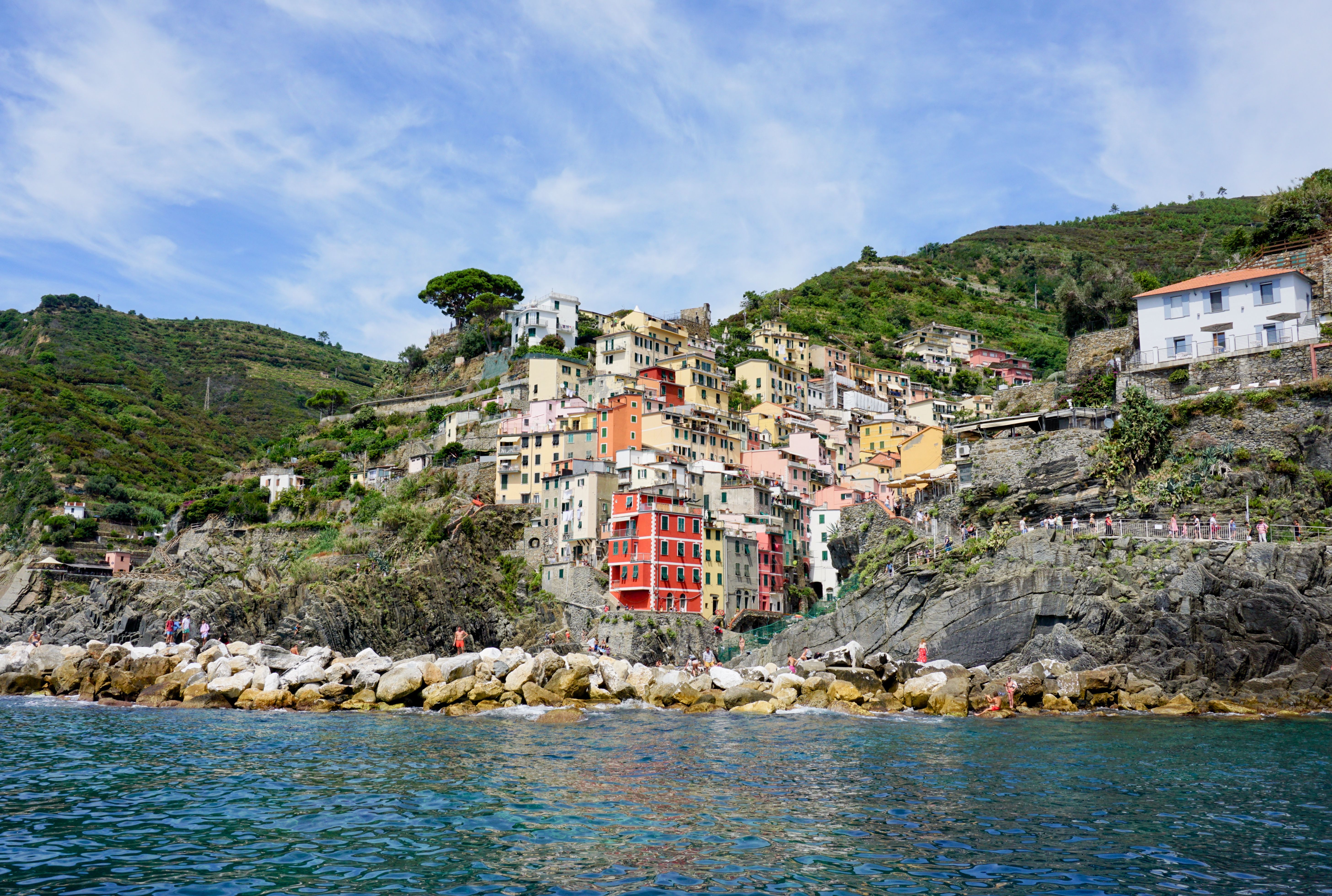 Steep coloured village houses above a rocky Ligurian harbour with fishing boats