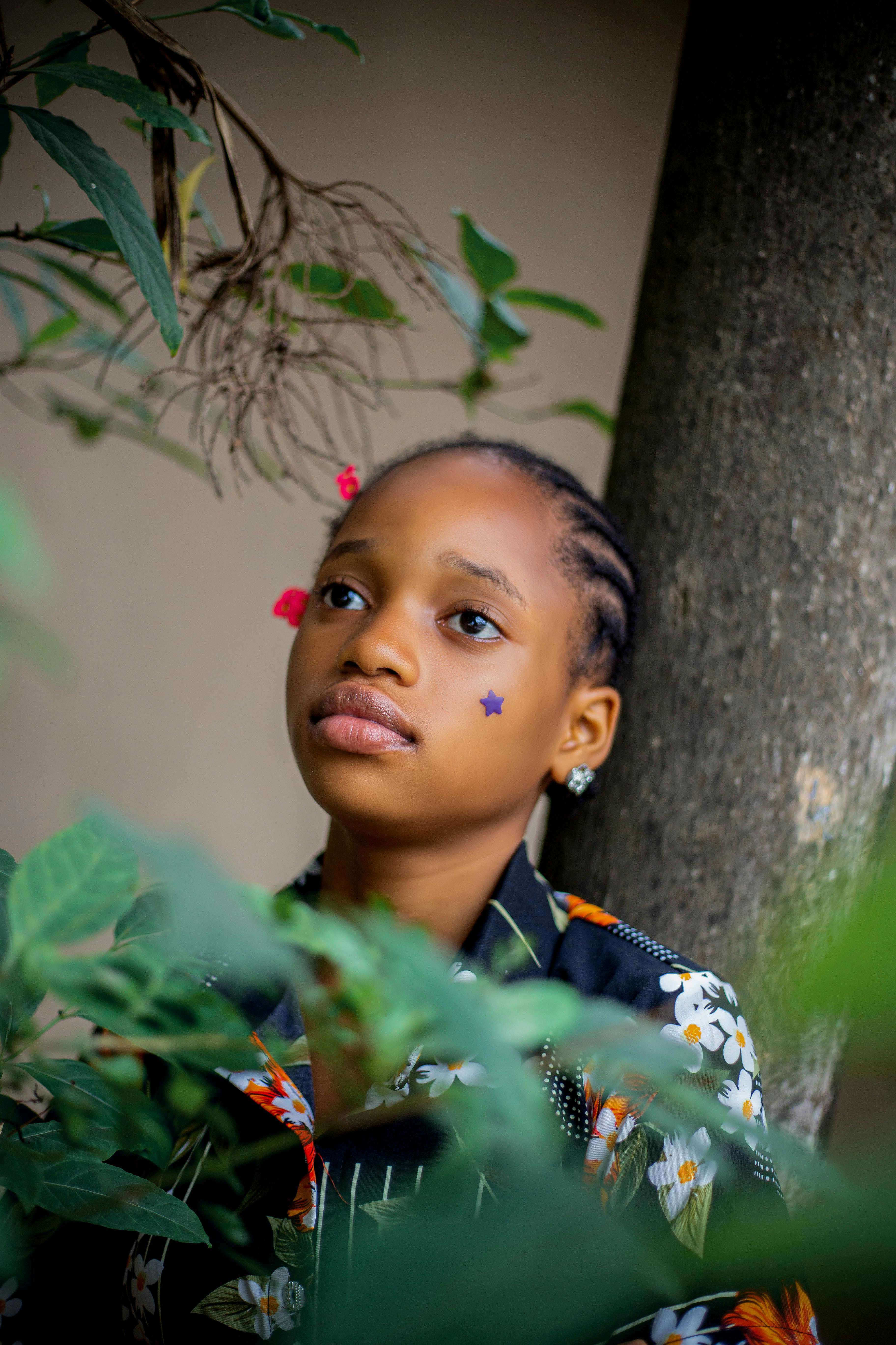 A contemplative young girl with a star sticker on her face amidst foliage, showcasing innocence.