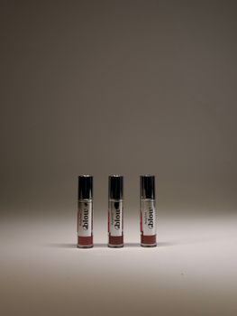 Three elegant lip gloss tubes with a minimalist aesthetic on a neutral background.