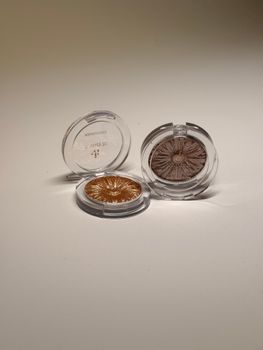 Two compact highlighter powders in gold and bronze shades on a white surface.