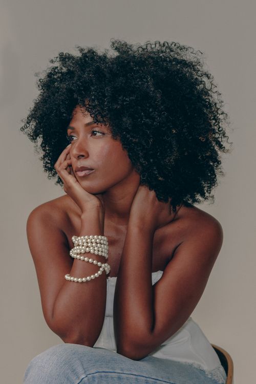 Free Elegant portrait of a woman with natural curls and pearl bracelets, deep in thought. Stock Photo