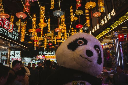 A bustling night scene in Guilin, China with colorful lanterns and a panda mascot entertaining the crowd.