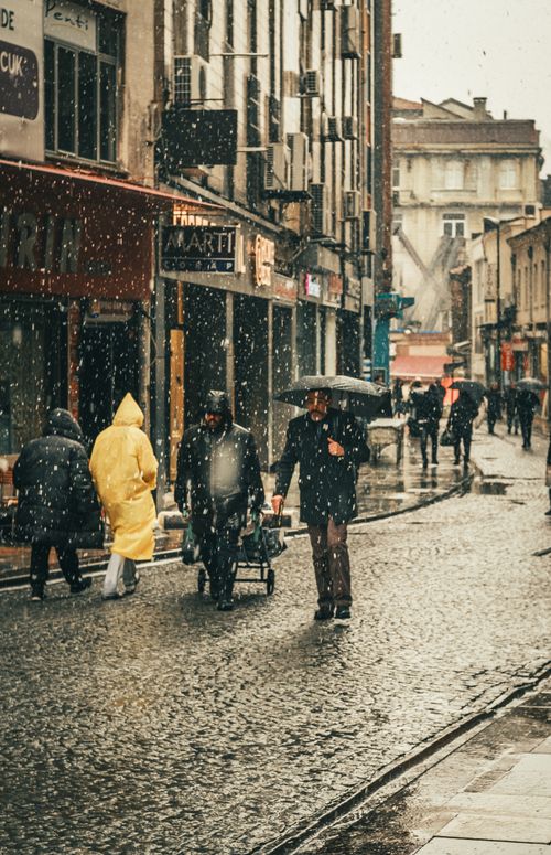 Free Pedestrians braving snowfall in a bustling urban street setting, capturing the hustle and city life. Stock Photo