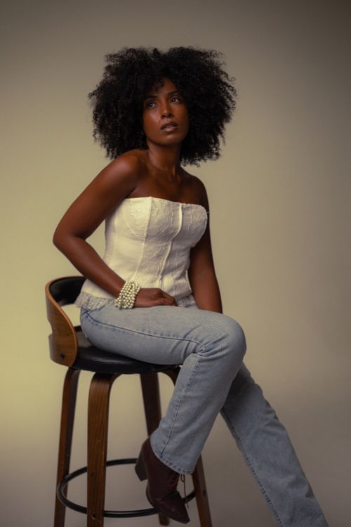 Free Stylish portrait of a woman with an afro hairstyle, sitting on a stool in a studio setting. Stock Photo