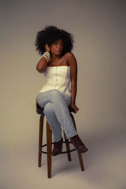 Free Elegant portrait of a woman with afro hair sitting on a stool in a studio setting. Stock Photo