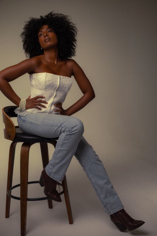 Free Sophisticated portrait of an African woman in casual chic attire seated on a wooden chair. Stock Photo