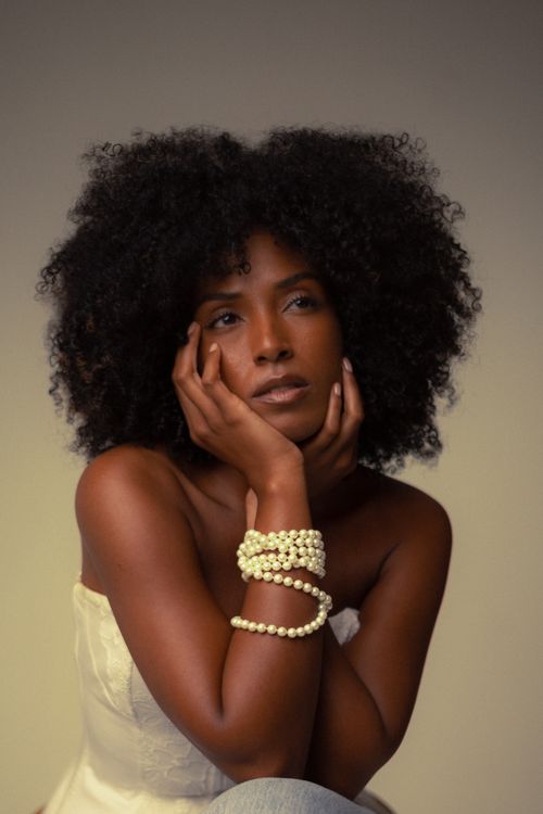 Free Graceful studio portrait of a woman with curly hair and pearl bracelets, exuding elegance. Stock Photo