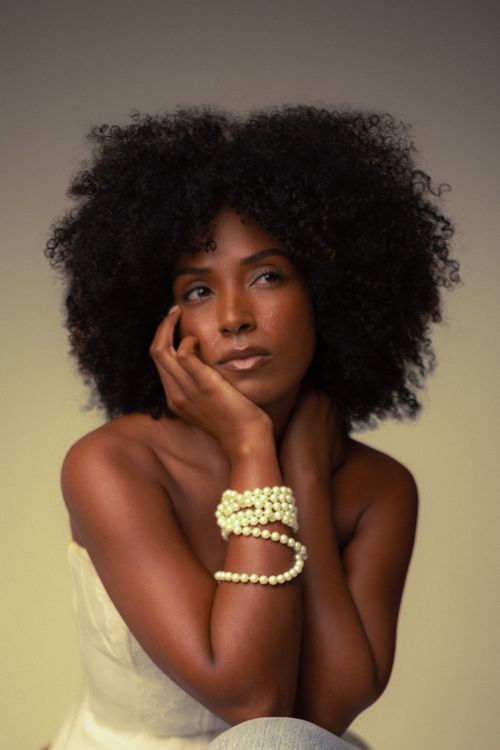 Free Thoughtful woman with natural curly hair and pearl jewelry in a studio setting. Stock Photo