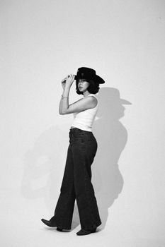 Artistic black and white portrait of a fashionable cowgirl posing in a studio setting.