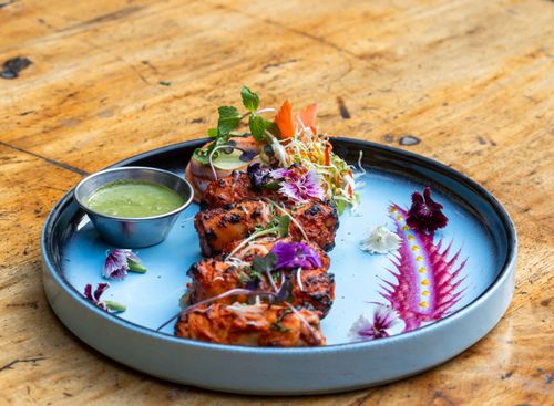 Free Delicious grilled chicken tandoori garnished with edible flowers and herbs on a rustic table. Stock Photo