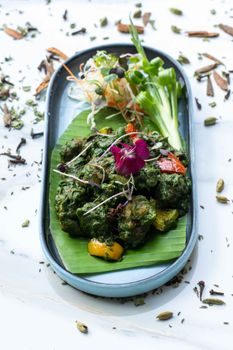 Vibrant plate of sautéed vegetables and edible flowers on a banana leaf, garnished with microgreens.