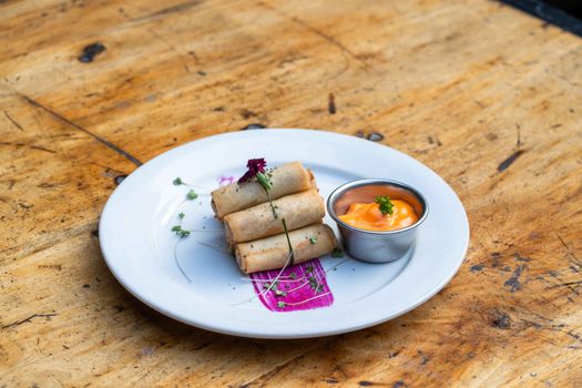 Crispy spring rolls with a tangy dipping sauce on a wooden table, garnished with herbs.