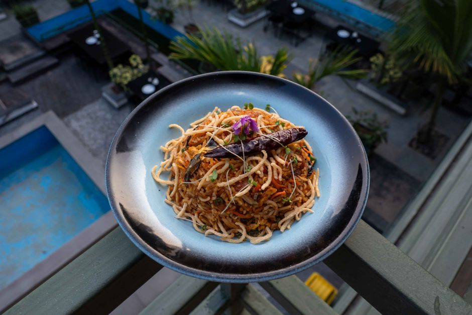 Plate of spicy noodles garnished with herbs and chili served outdoors on a balcony.