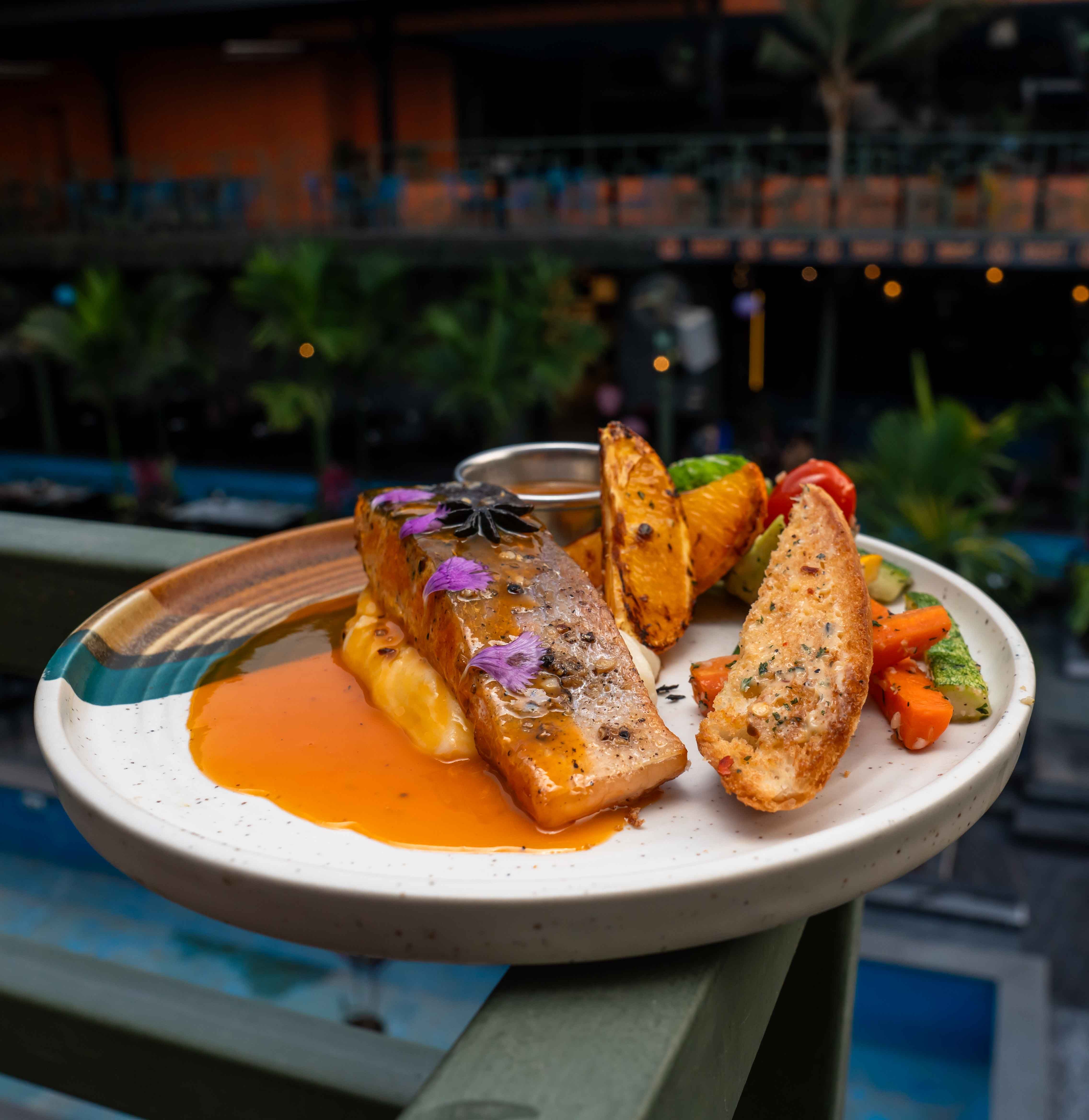 Delicious grilled salmon with roasted vegetables and sauce served on a balcony.