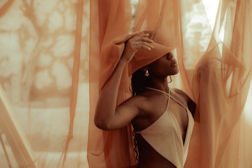 Free A serene portrait of a woman in neutral tones posed behind flowing orange fabric. Stock Photo