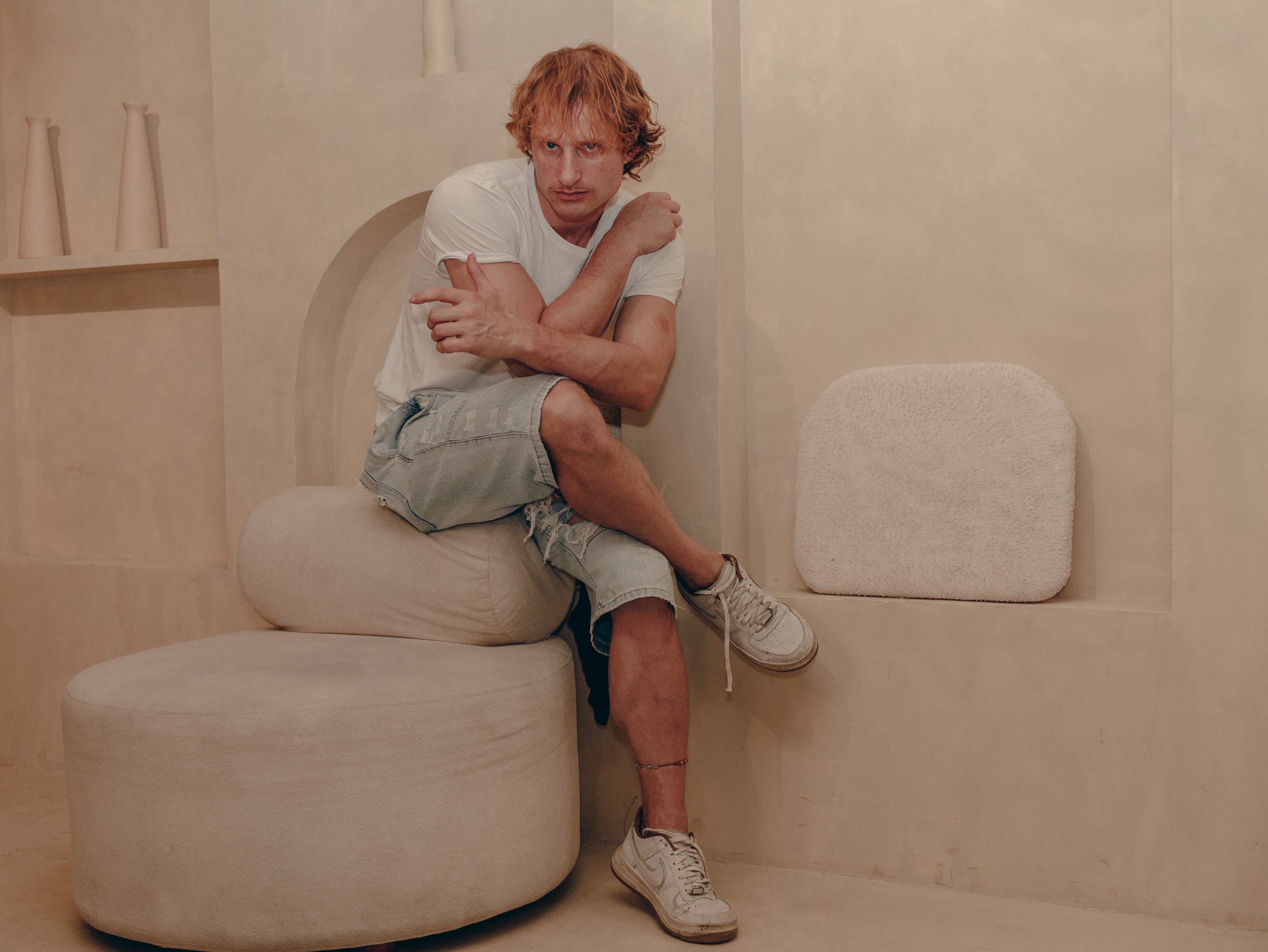 Man in casual outfit sitting on modern furniture in a beige minimalist room.