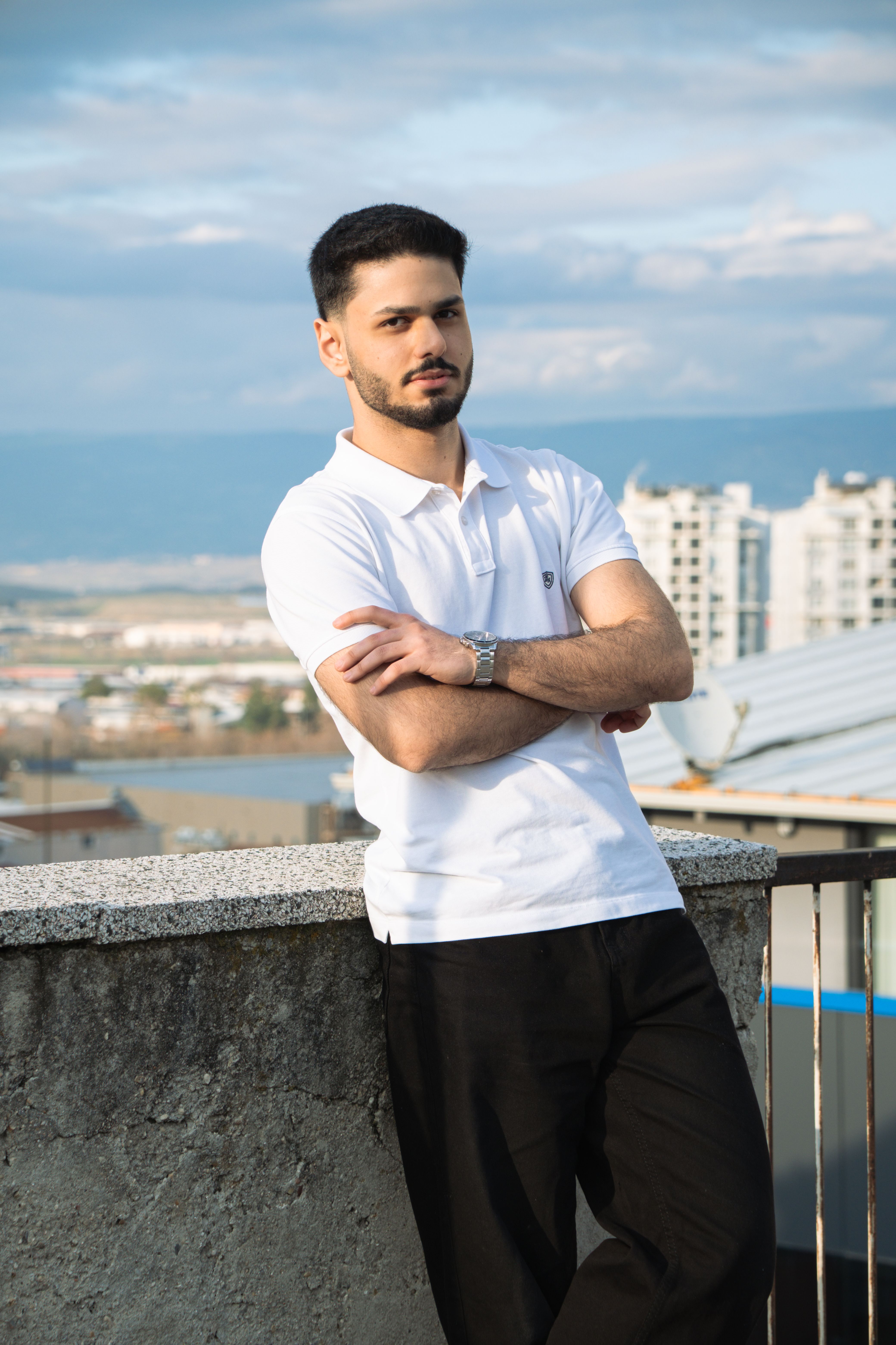 Young man in white shirt leaning on rooftop ledge with cityscape background.