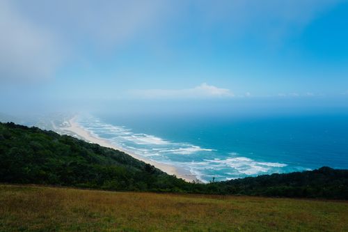 Free Stunning panoramic view of a coastline with lush greenery and blue ocean waves under a bright sky. Stock Photo