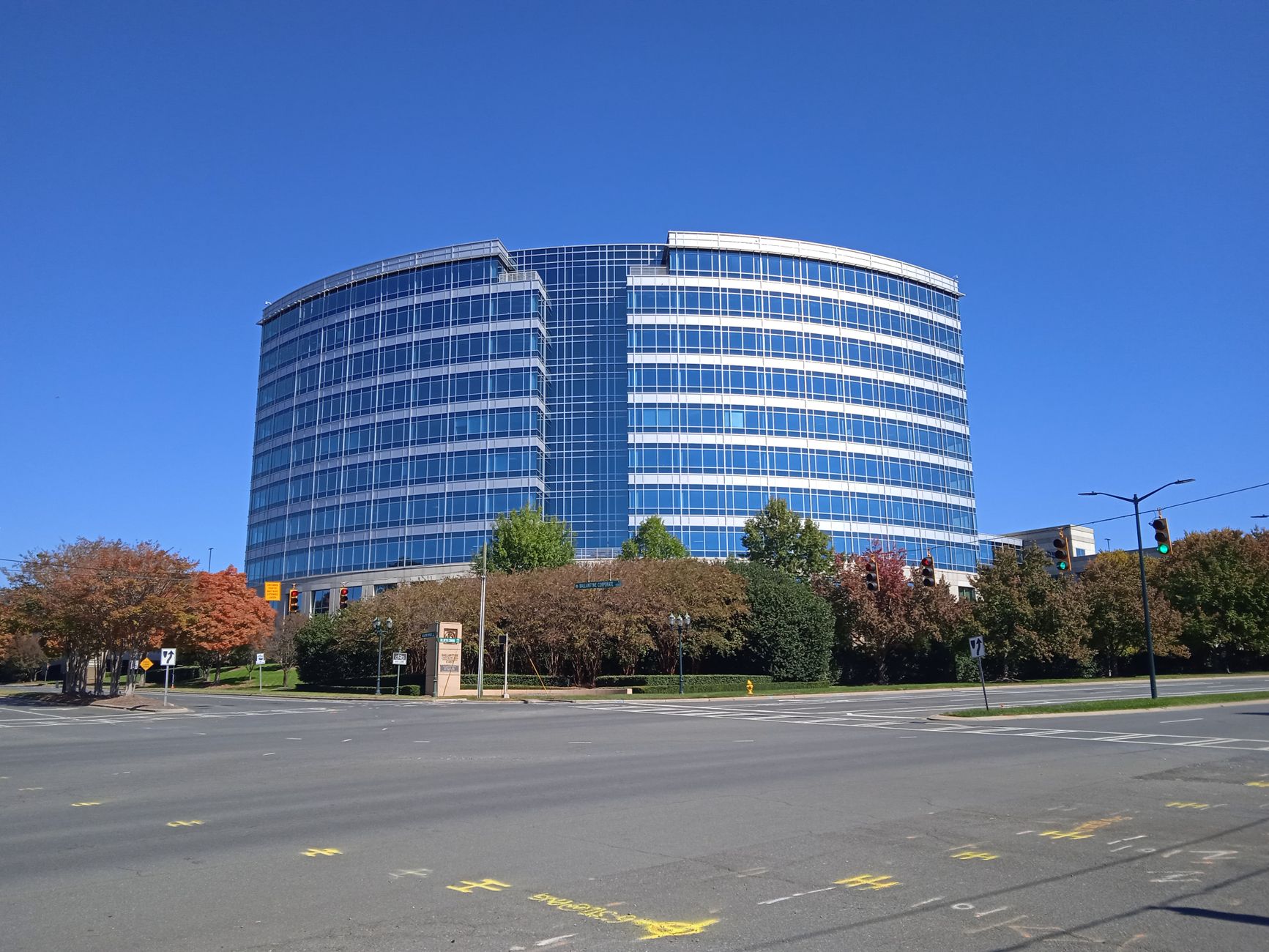 A curved glass office building with a blue sky backdrop, surrounded by autumn trees.