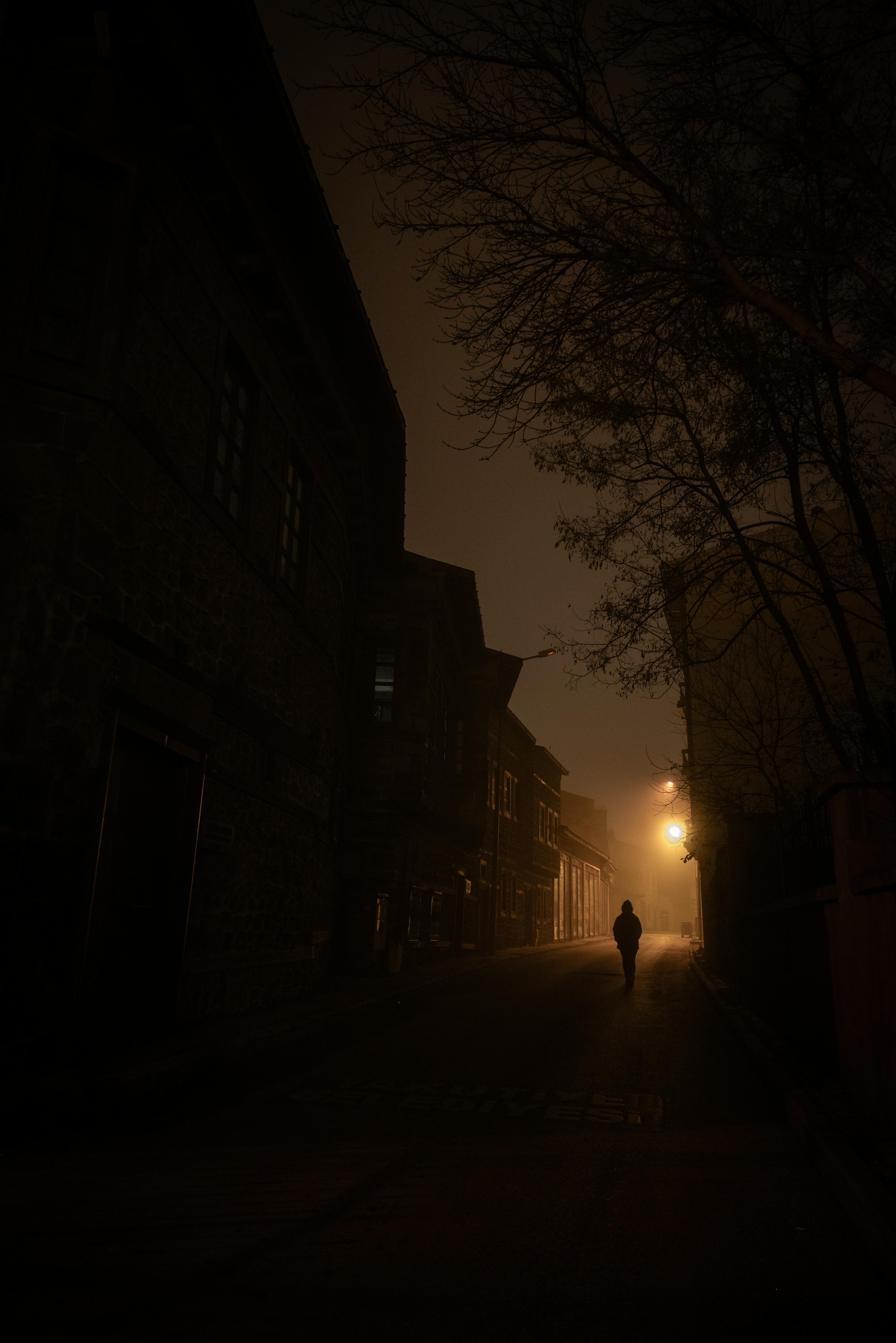 A solitary figure walks down a dimly lit street at night, enveloped in an atmospheric urban setting.