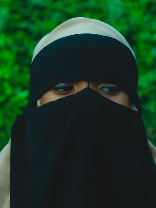 Free A close-up portrait of a woman wearing a black niqab, set against a green leafy background. Stock Photo