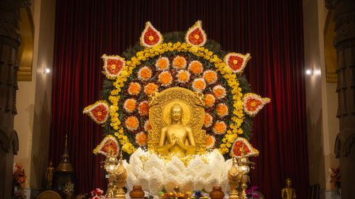 Free Golden Buddha statue with vibrant floral mandala backdrop in an ornate indoor setting. Stock Photo