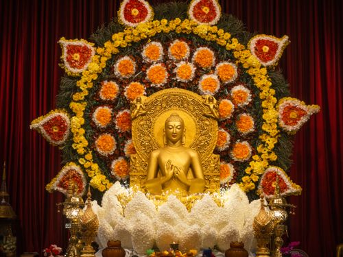 Free A golden Buddha statue surrounded by vibrant floral decorations and lanterns against a red backdrop. Stock Photo