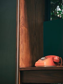A vintage orange rotary phone sits on a wooden shelf against a dark green background, offering a nostalgic touch.