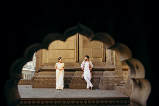 A couple in traditional attire stands inside a historic monument, captured in an artistic frame.