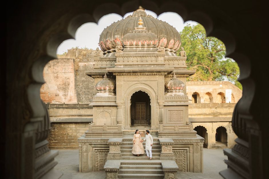 A couple stands at a historic temple surrounded by intricate stonework and lush greenery.