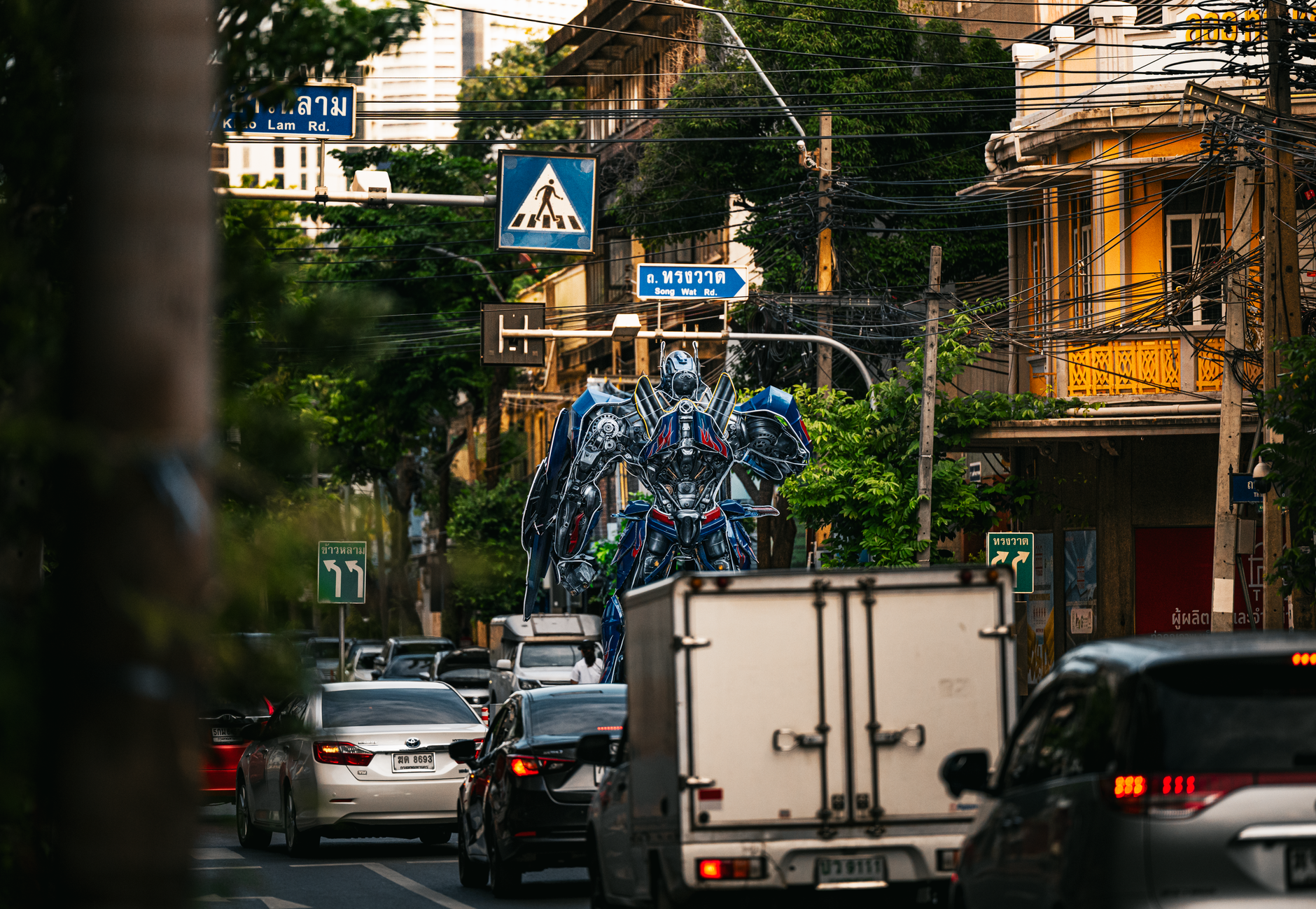 A large robot statue dominates the traffic scene in a bustling Bangkok street.