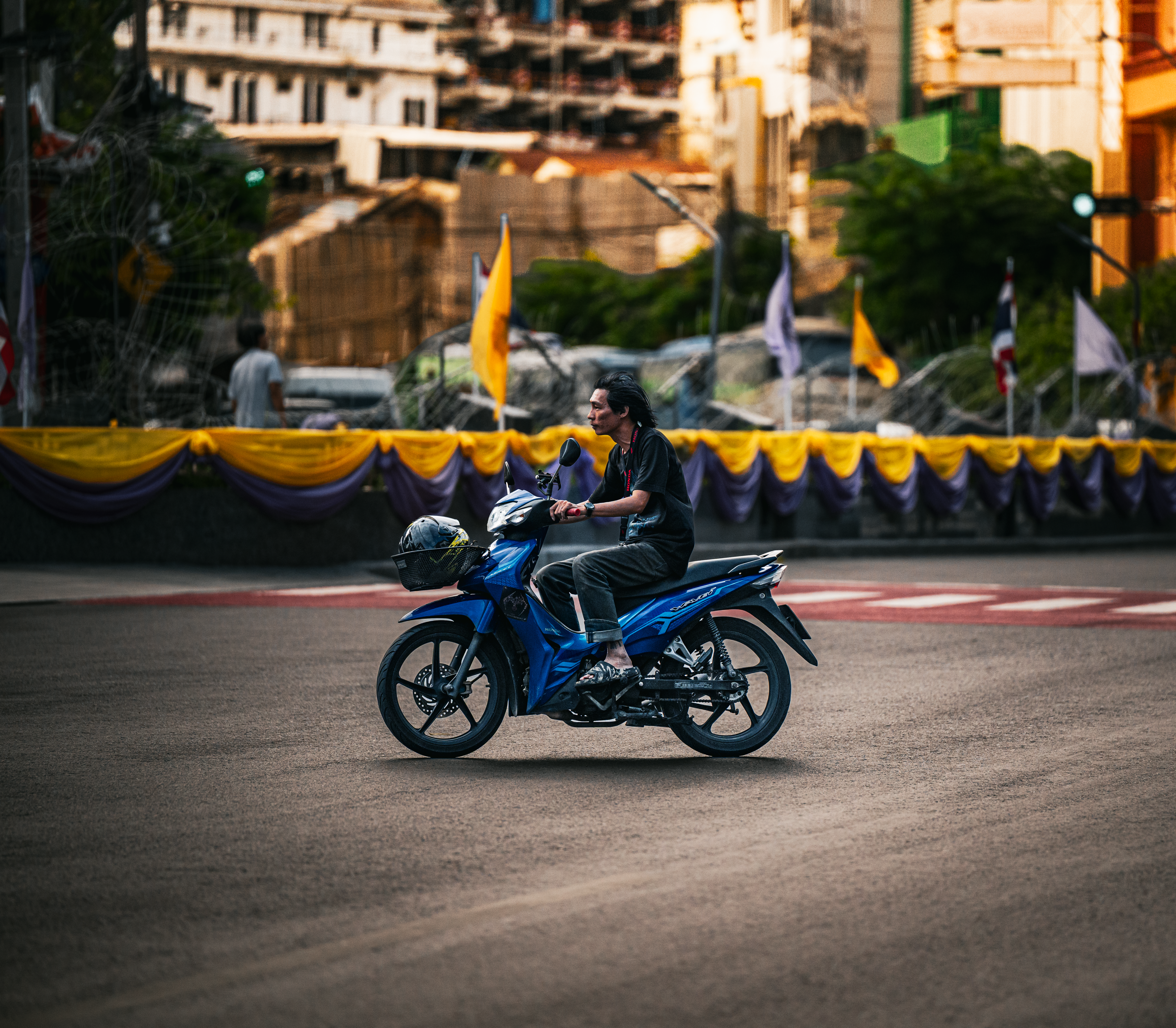 A man rides a blue motorbike through a decorated street in Bangkok, Thailand.