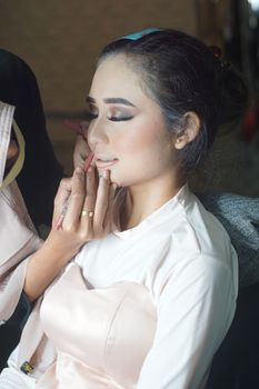 A bride from Indonesia having makeup applied in preparation for her wedding ceremony. - Fotografer Sidoarjo