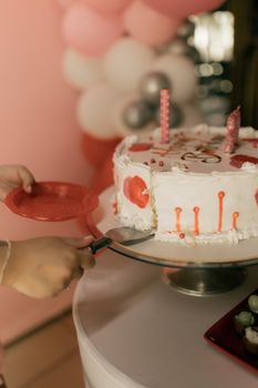 Hands cutting a decorated birthday cake with pink candles indoors.