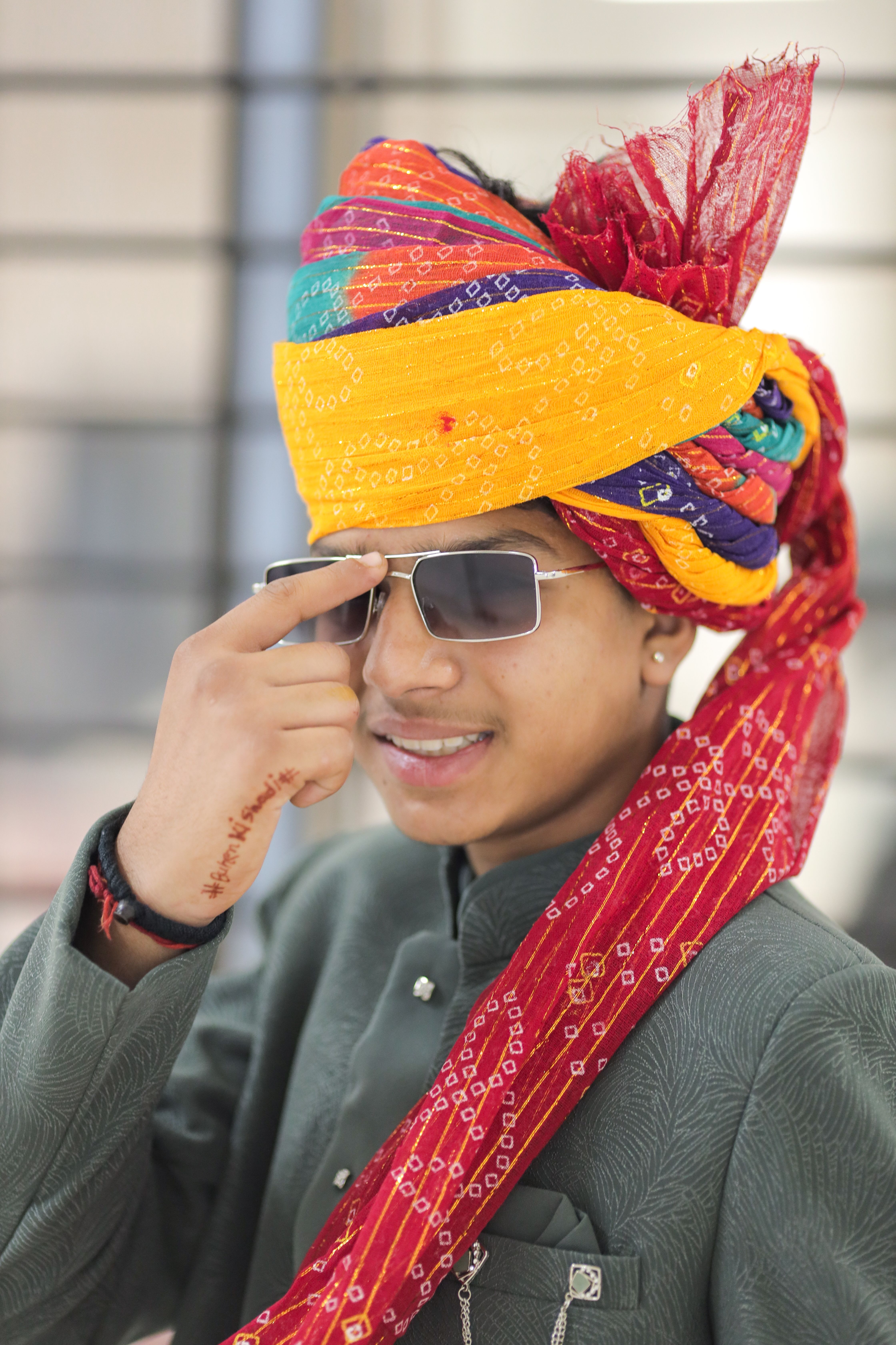 Young man in traditional Indian attire and colorful turban wearing stylish sunglasses indoors.