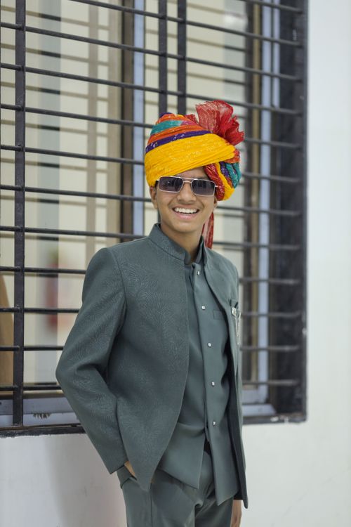Free Portrait of a young man in a traditional colorful turban and modern suit, smiling indoors. Stock Photo