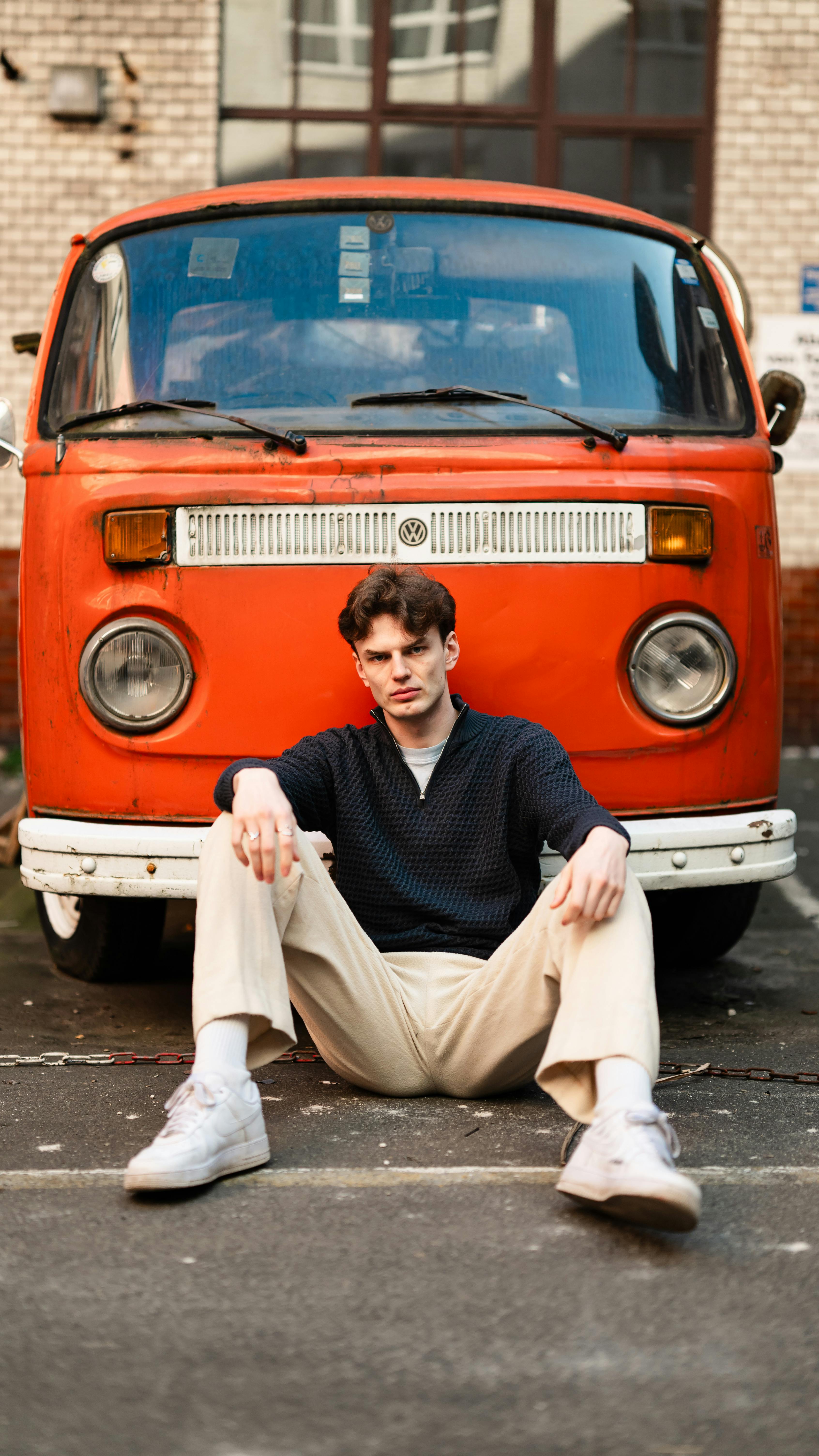 Stylish young man sitting in front of a classic orange van in Berlin's urban setting.
