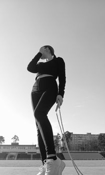 Black and white image of woman exercising with jump rope outdoors.
