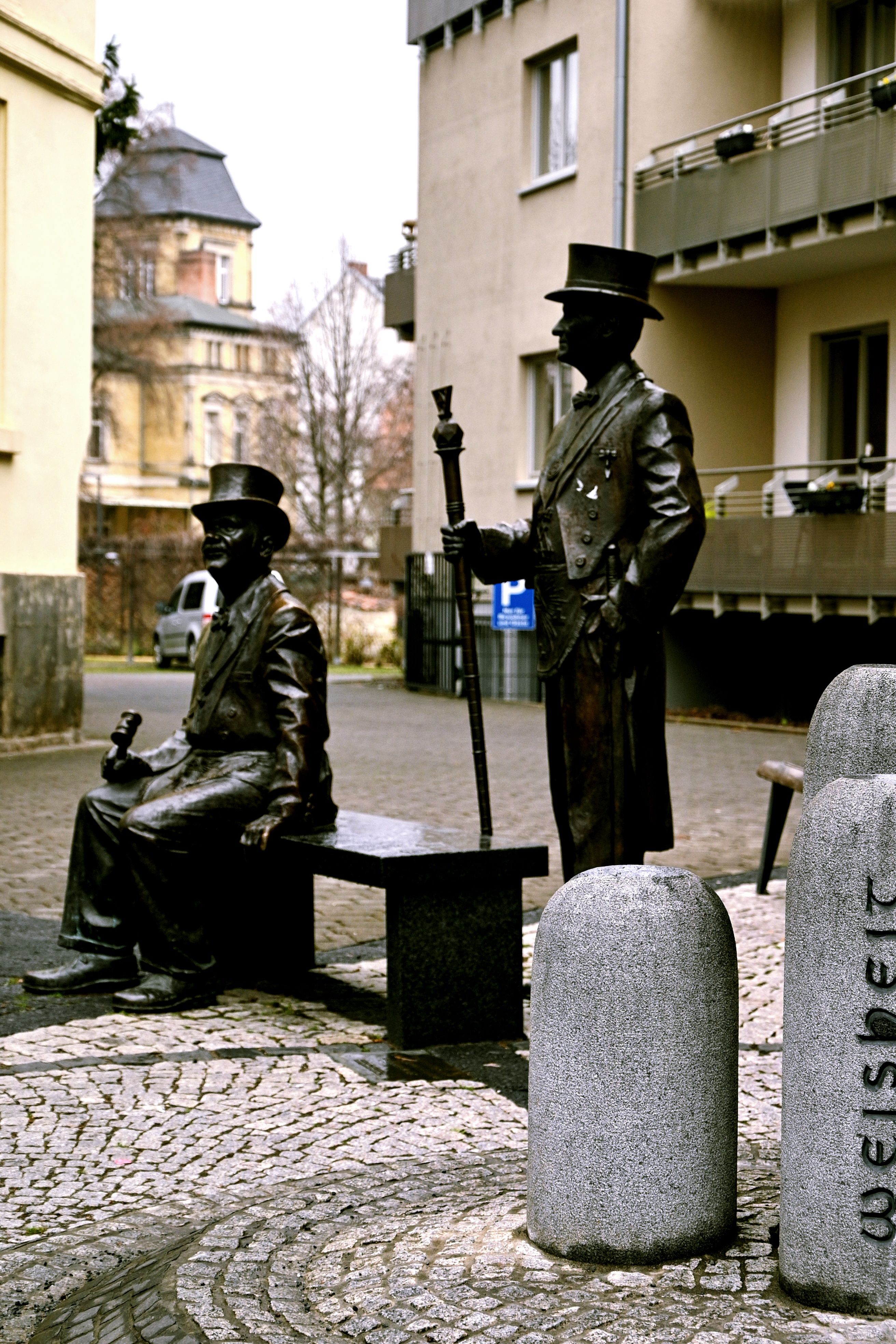 Two bronze statues of men in traditional attire on a cobblestone street in Quedlinburg, Germany.