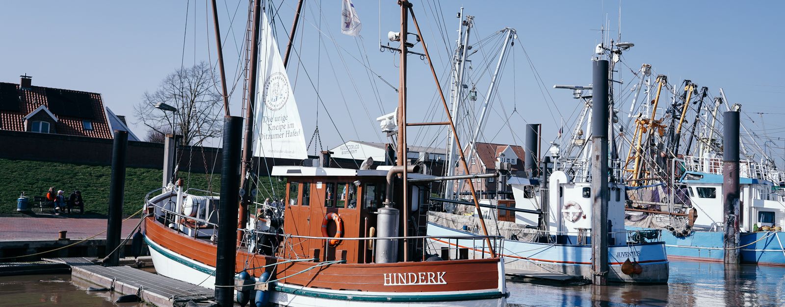 Scenic view of wooden fishing boats docked in Emden, Germany harbor on a sunny day.