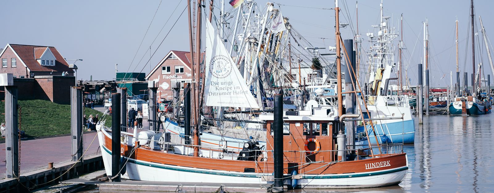 Traditional fishing boats docked at a harbor in Emden, Germany on a sunny day.