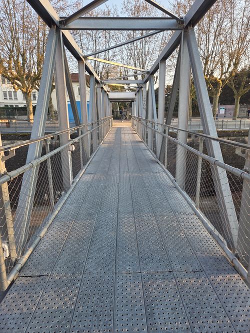 Free View of a modern steel pedestrian bridge with trees lining the pathway. Stock Photo