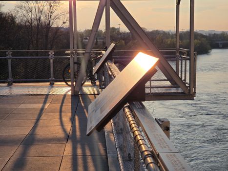 A serene view of a sunlit bridge with river and informational panels during sunset.