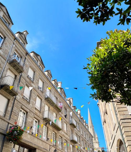 Free Beautiful street view in Saint-Malo, France, with colorful flags, traditional architecture, and a bright blue sky. Stock Photo