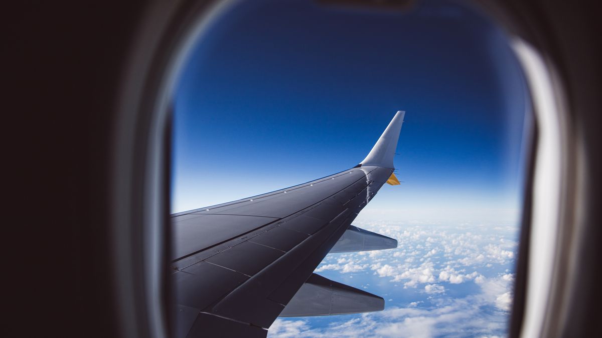 A view from an airplane window showing the wing and clouds below, captured in daylight.